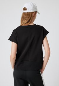 Zwart sweatshirt met korte mouwen en een ronde hals, met een gladde textuur en een iets losse pasvorm. Inclusief een naad aan de achterkant.