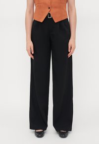Black wide-leg pants with a smooth texture, featuring a high waist and front pleats. Paired with an orange fitted vest, with minimalistic design.