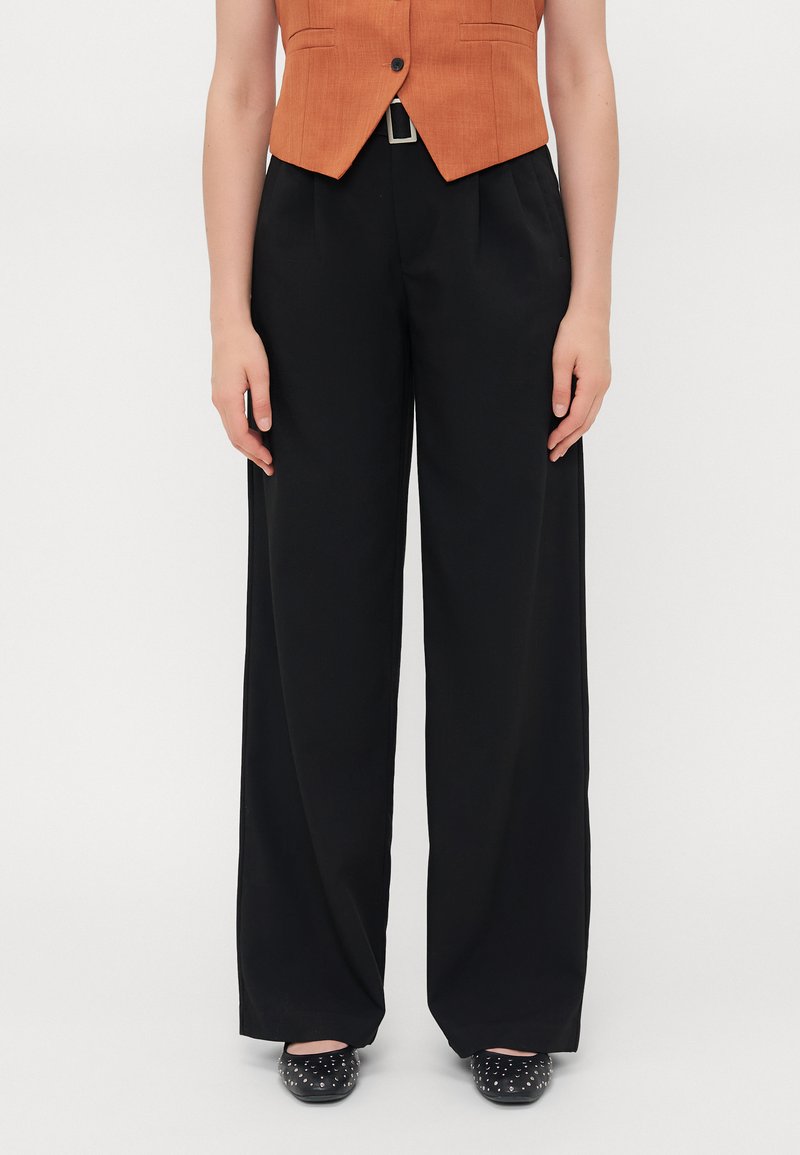 Black wide-leg pants with a smooth texture, featuring a high waist and front pleats. Paired with an orange fitted vest, with minimalistic design.