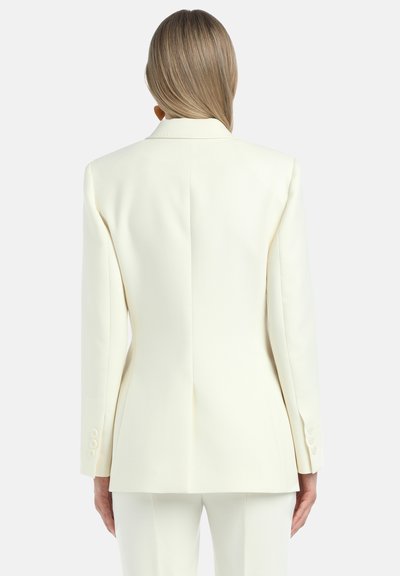 Biały żakiet na miarę z wyraźną strukturą, długimi rękawami i mankietami na dwa guziki. Gładki materiał z eleganckim wycięciem na plecach.