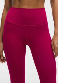 Legginsy o wysokim stanie w jasnofioletowej tkaninie o gładkiej fakturze, z bezszwowym pasem i minimalnymi detalami szycia.