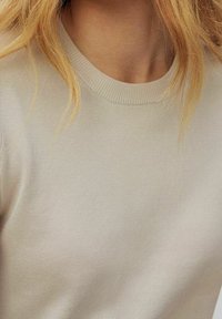 Suéter beige claro con cuello redondo, textura de fino canalé y mangas cortas, que muestra una tela suave sin patrones ni acentos visibles.