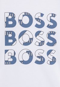Balta T-marškiniai su „BOSS“ užrašu mėlyna ir juoda spalvomis. Užrašas turi įvairius raštus, įskaitant vientisus, juostuotus ir geometrinius formas.