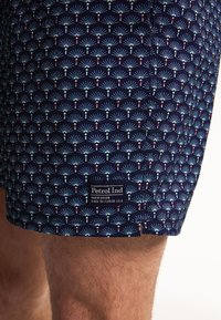 Námořnické plavky s opakujícím se vzorem modrých a červených fanoušků. Obsahují štítek s textem "Petrol Ind" na straně.