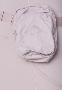 Lichtgrijze ritstas met een ruitpatroon en een dieptegestempeld logo, bevestigd aan een bijpassende stoffen riem, die een zachte, gestructureerde oppervlakte toont.