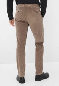 Bruine corduroy broek met verticale ribbels en twee achterzakken, gecombineerd met zwarte veterschoenen.