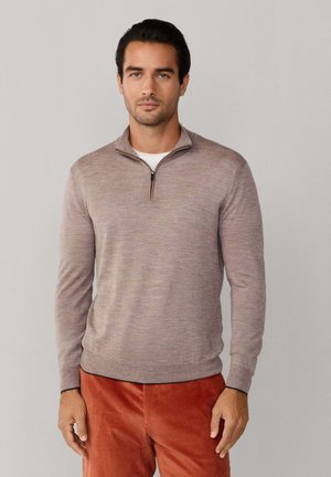 Suéter marrón con cuello de cremallera, material de punto ligero, de mangas largas, con dobladillo acanalado, costura personalizada, usado sobre una camiseta blanca, combinado con pantalones de pana naranja.