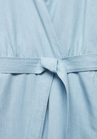Vêtement en tissu bleu clair avec une ceinture cousue nouée en un nœud lâche au niveau de la taille.