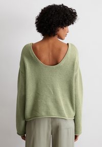 Hellgrüner, übergroßer Pullover aus strukturiertem Strick, mit weitem Ausschnitt und offenem Rückendesign. Kombiniert mit hellgrünen, locker sitzenden Hosen.