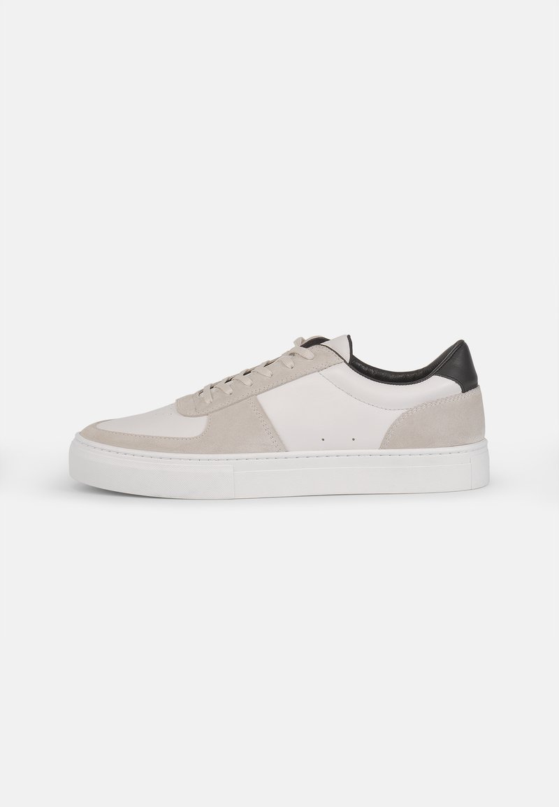 Sneakers mit einer glatten weißen Gummisohle, beigem Wildleder und Lederakzenten. Sie besitzen eine abgerundete Zehenpartie, flache Schnürsenkel und seitliche Perforationen.
