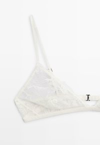 Hvid blondetop med tynde justerbare stropper og en sort hægtekrog-lukning på hvid baggrund.