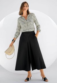 Bloes met bloemenprint in wit en zwart, hoge zwarte culottes, zwarte hakken sandalen en een crèmekleurige handtas. Soepele texturen, relaxte pasvorm.