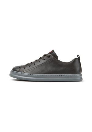 Zapatilla baja negra de cuero con suela gris, cordones delanteros y tira en el talón, mostrada de lado sobre fondo blanco.