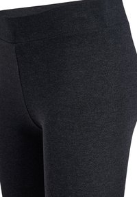 Zbliżenie na czarną, rozciągliwą tkaninę legginsów z wysokim pasem i gładkimi detalami szwów.