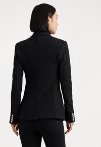 Zwarte tailormade blazer met een hoge kraag, lange mouwen en zilverkleurige knoopaccenten op de manchetten. Gladde textuur en een aansluitend ontwerp.