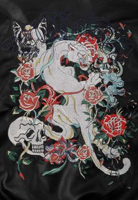 Pelle nera con ricami intricati raffiguranti un giaguaro bianco, rose rosse, un teschio e motivi vorticosi; colori vivaci e texture dettagliate.