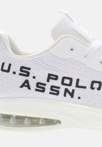 Fehér sportcipő, hálós felsőrésszel, párnázott talppal, és a "U.S. POLO ASSN." fekete logója hangsúlyosan látható az oldalán.