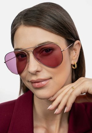 Rosa-tonede aviator solbriller med tynde metalliske stel. Modellen bærer en bordeauxjakke, der viser en guldring og en delikat ring.