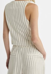 Bezramenný béžový top s vertikálními šedými pruhy, s krátkým střihem, elastickým pasem a dvěma zadními kapsami.