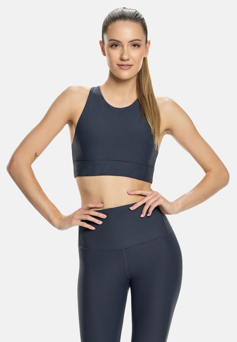 Tumši pelēkā sporta krūšturis un augsto vidukļa legingi, izgatavoti no gludas, elastīgas auduma, ar vienkāršu dizainu bez rakstiem vai logo.