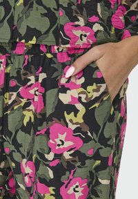 Blommig jumpsuit med en blandning av rosa och gröna blommor mot en svart bakgrund, med resårmidja och diskreta sidfickor.