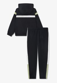 Μαύρο αθλητικό σετ φόρμας που περιλαμβάνει μπουφάν με κουκούλα και ριγέ λευκές και ανοιχτοπράσινες λεπτομέρειες, καθώς και αντίστοιχα στενά παντελόνια με λευκές πλάγιες λεπτομέρειες.