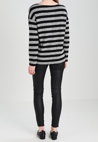 Zwart en grijs gestreepte sweater met een relaxed fit, gecombineerd met strakke zwarte neplederen broek en zwarte instapschoenen.