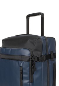Marineblauwe reistas op wielen met een getextureerd zwart bovenstuk, meerdere ritsen, verstelbare riemen en een uitschuifbare handgreep voor eenvoudig transport.