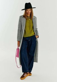 Šedý kabát s houndstooth vzorem, olivově zelený svetr, široké modré džíny, hnědé tenisky se pruhy, růžová kabelka, černý klobouk s širokým okrajem.