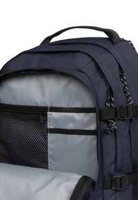 Granatowy plecak z szarym wnętrzem; posiada siatkowaną kieszeń, wiele przegródek oraz regulowane paski, wykonany z trwałej tkaniny.