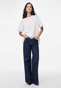 Hvit t-skjorte med korte ermer kombinert med høyt liv, vidde mørkeblå jeans. Antrekket har en avslappet passform og minimalisk design.