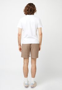 Witte shirt met korte mouwen, beige shorts en lichtgekleurde sneakers; achteraanzicht dat een minimale stijl en casual pasvorm toont.