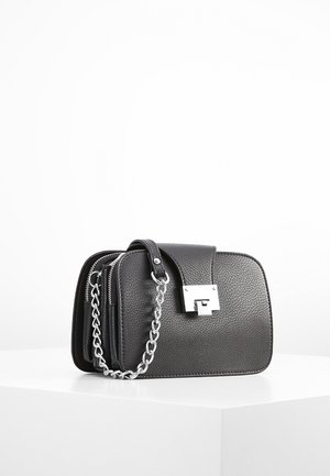 Sac bandoulière en cuir noir texturé avec bandoulière chaîne argentée et fermoir carré argenté sur une surface blanche.