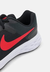 Czarne sportowe buty z teksturowaną siateczką u góry, czerwonym logo Nike, wyściełanym kołnierzem i białą, amortyzowaną podeszwą. Gumowa podeszwa dla lepszej przyczepności.