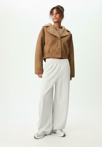 Hnědá umělá sukně z semiše, zkrácená, s béžovým kožíškem na límci a zapínáním na knoflík, spárovaná se šedými širokými kalhotami na volno a stříbrnými teniskami.