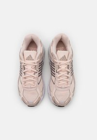 Par svetlo roza Adidas tekaških čevljev z mrežasto in semiš teksturo, črnimi črtami in vezalkami, gledano z vrha na belo ozadje.