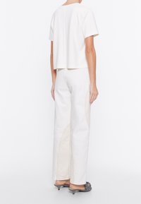 Top bianco accorciato con maniche corte, abbinato a pantaloni bianchi a vita alta con cuciture beige a contrasto e un dettaglio laterale.