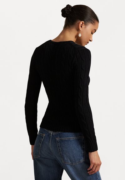 Black cable-knit sweater with long sleeves, featuring a ribbed hem and detail on the arms. Paired with medium-wash blue jeans.