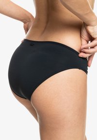 Bas de bikini taille haute noir avec une texture lisse, une taille élastique et des détails de couture minimaux, conçu pour le confort et l'ajustement.