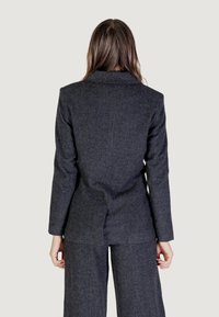 Blazer su misura grigio scuro con rever a punte, vestibilità strutturata e una texture sottile, abbinato a pantaloni coordinati per un look coerente.