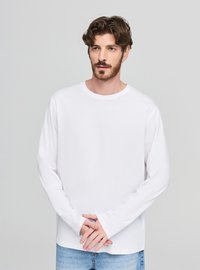 Biała bawełniana koszula z długim rękawem, okrągłym dekoltem, luźnym krojem i lekko wydłużonymi mankietami. Styl casualowy w połączeniu z jasnoniebieskimi denimowymi spodniami.