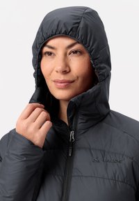 Zwarte gewatteerde jack met een capuchon, voorzien van een ritssluiting aan de voorkant en elastische manchetten. Heeft een gladde textuur en een subtiele merklogo op de borst.