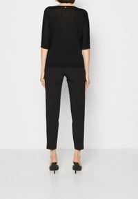 Zwarte, lichtgewicht blouse met korte mouwen en een boothals, gecombineerd met op maat gemaakte zwarte broek en zwarte pumps met hak.