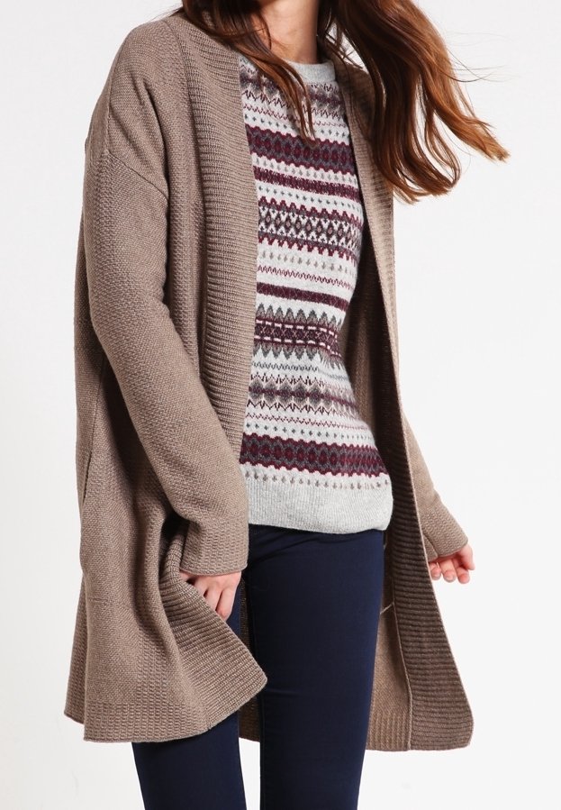 Femme portant un pull en maille à motifs bordeaux et gris sous un long cardigan marron ouvert, associé à un pantalon sombre.