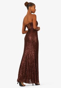 Abito lungo senza spalline in un ricco tessuto bronzeo scintillante. Presenta una schiena con lacci e una silhouette aderente e liscia con paillettes.