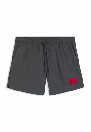 Bañador corto para hombre de color gris oscuro con cinturilla elástica, cordón ajustable, bolsillos laterales y un parche rojo con la palabra "HUGO" en la pierna izquierda inferior.
