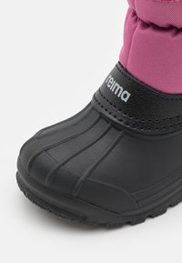 Stivale nero impermeabile con suola rigata e parte superiore imbottita rosa; presenta una cinghia regolabile con il nome del marchio in bianco.