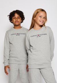 Szürke kereknyakú pulóverek bordázott mandzsettával, "TOMMY HILFIGER EST. 1985" felirattal sötét betűkkel a mellkason. Puha anyag, laza szabás.
