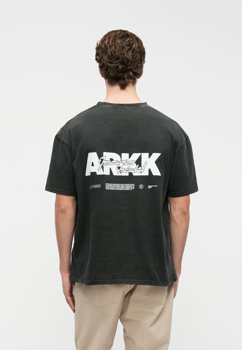 T-shirt de algodão cinza escuro com um corte boxy, apresentando gráficos e texto de logotipo brancos nas costas. Mangas curtas e decote redondo.