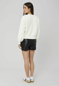 Pull blanc duveteux, short en cuir noir texturé, baskets blanches avec une bande noire, mannequin de dos, montrant les détails de l'encolure et du dos.